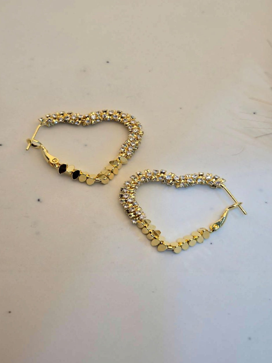 Pair of gold-plated heart hoop earrings with crystal stones laid flat on a white surface
