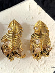 Pair of gold-plated feather stud earrings with champagne cubic zirconia stones on a white display surface