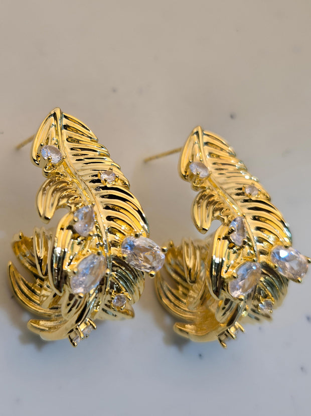 Close-up side view of gold-plated feather earrings showing sculpted barb detail and clear zirconia clusters