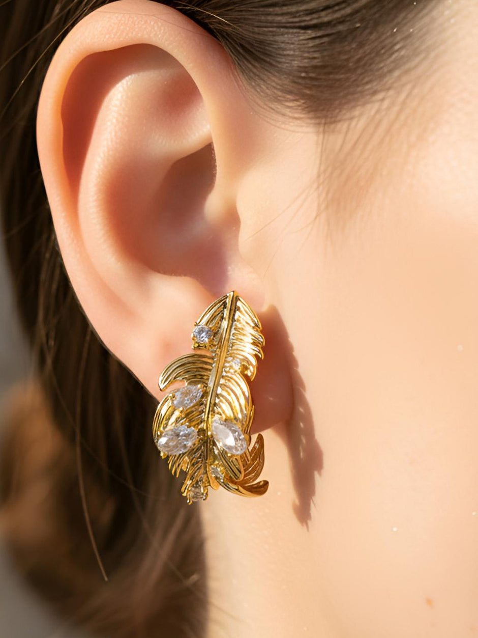 Gold-plated feather stud earring worn on a model's ear showing scale and fit against the lobe