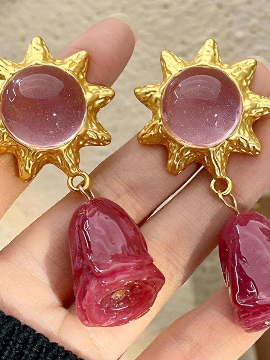 Gold sun drop earrings with pink stones and deep rose resin charms held in an open palm showing front detail