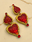 Pair of gold-tone double heart drop earrings with red resin inserts and crystal accents on a beige marble surface