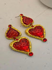 Both gold-tone red resin heart drop earrings laid flat on a white marble surface showing textured frame detail