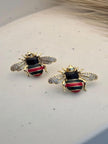 Pair of gold-plated bee stud earrings with red and green enamel abdomen and crystal wings on white surface