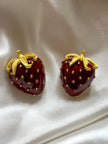 Pair of red enamel strawberry stud earrings with gold-plated leaves on white satin fabric