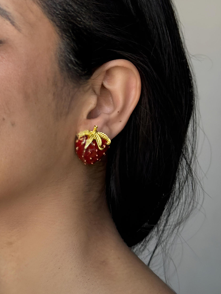 Red enamel strawberry stud earring worn on a woman's ear showing scale and fit