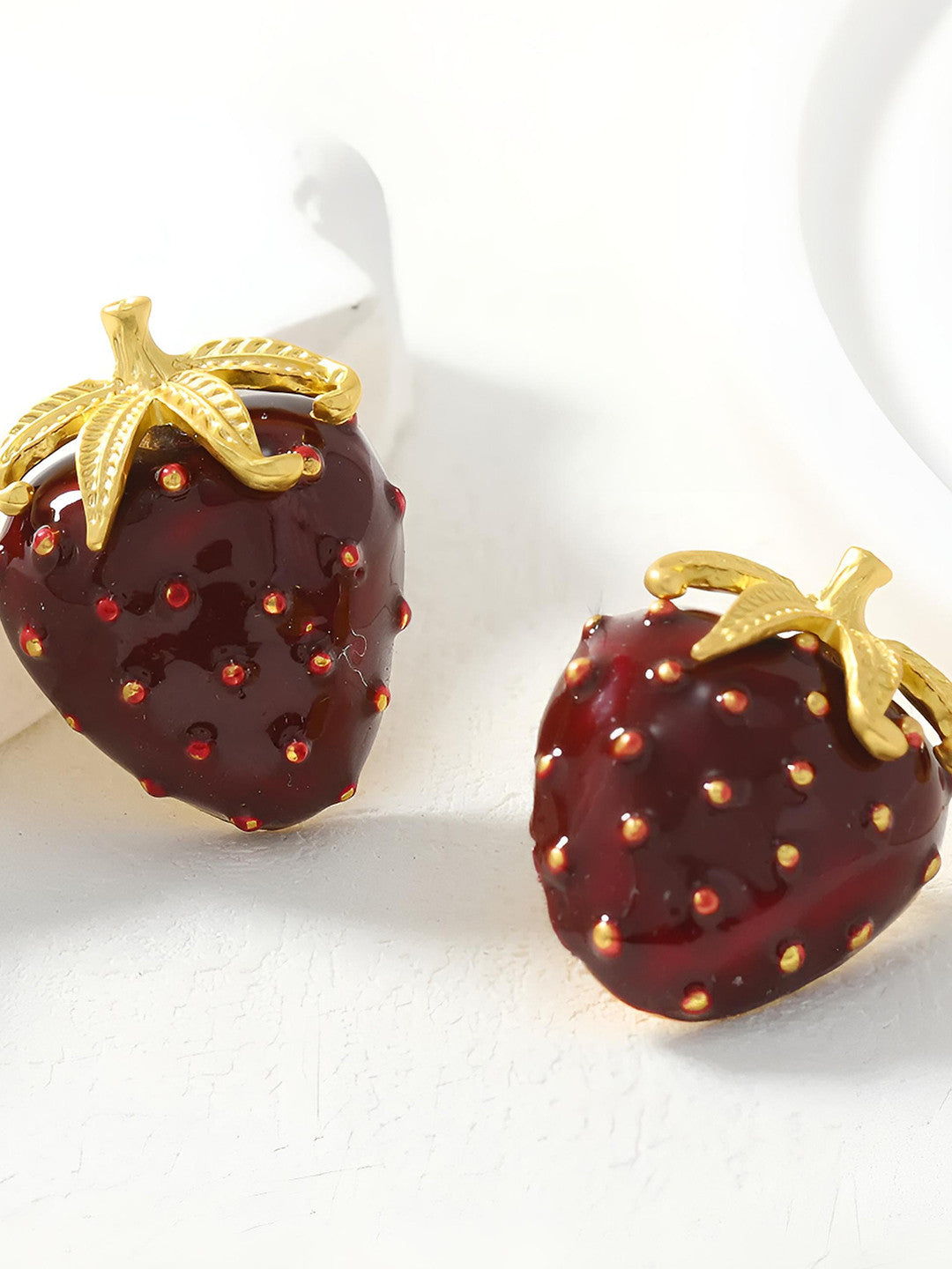 Close-up front view of two red enamel strawberry earrings with raised gold seed detailing and textured leaves