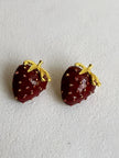 Side angle of red enamel strawberry stud earrings showing three-dimensional depth of the fruit body