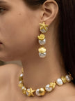 Model wearing gold sea shell drop earrings with a matching baroque pearl choker necklace, side profile view