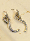 Two gold pavé snake drop earrings displayed on a beige textured surface showing coiled body detail