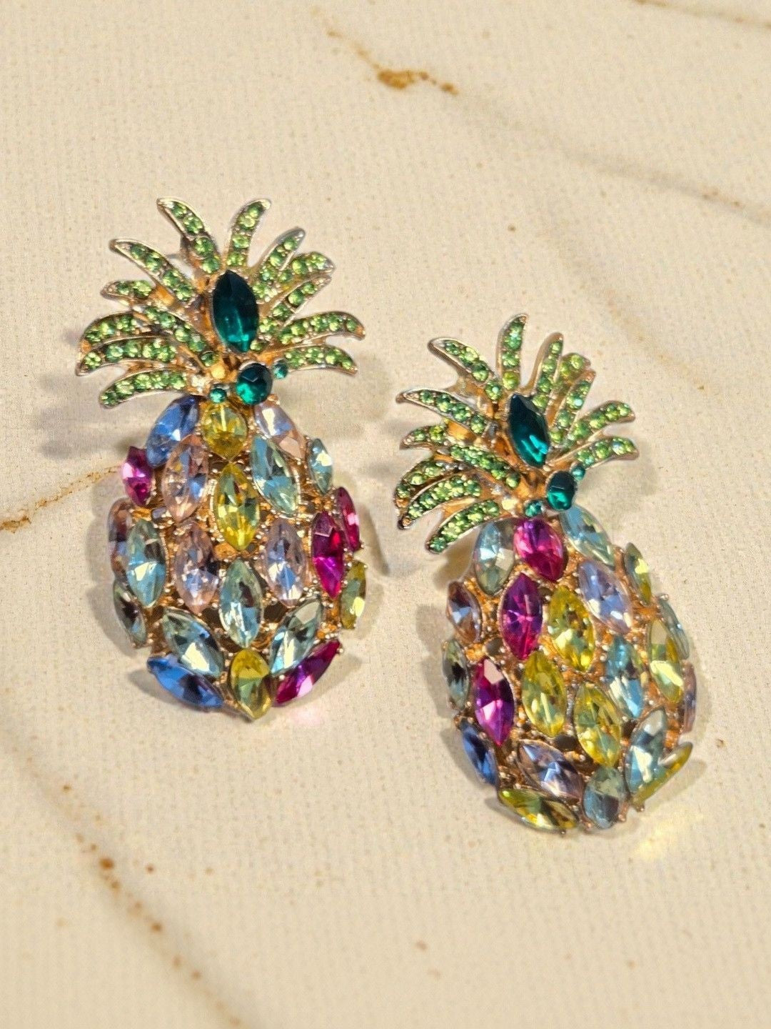Close-up of both multicolour Austrian crystal pineapple earrings on a marble surface showing stone detail
