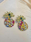 Top-down view of gold-plated pineapple crystal earring pair on a white speckled ceramic plate
