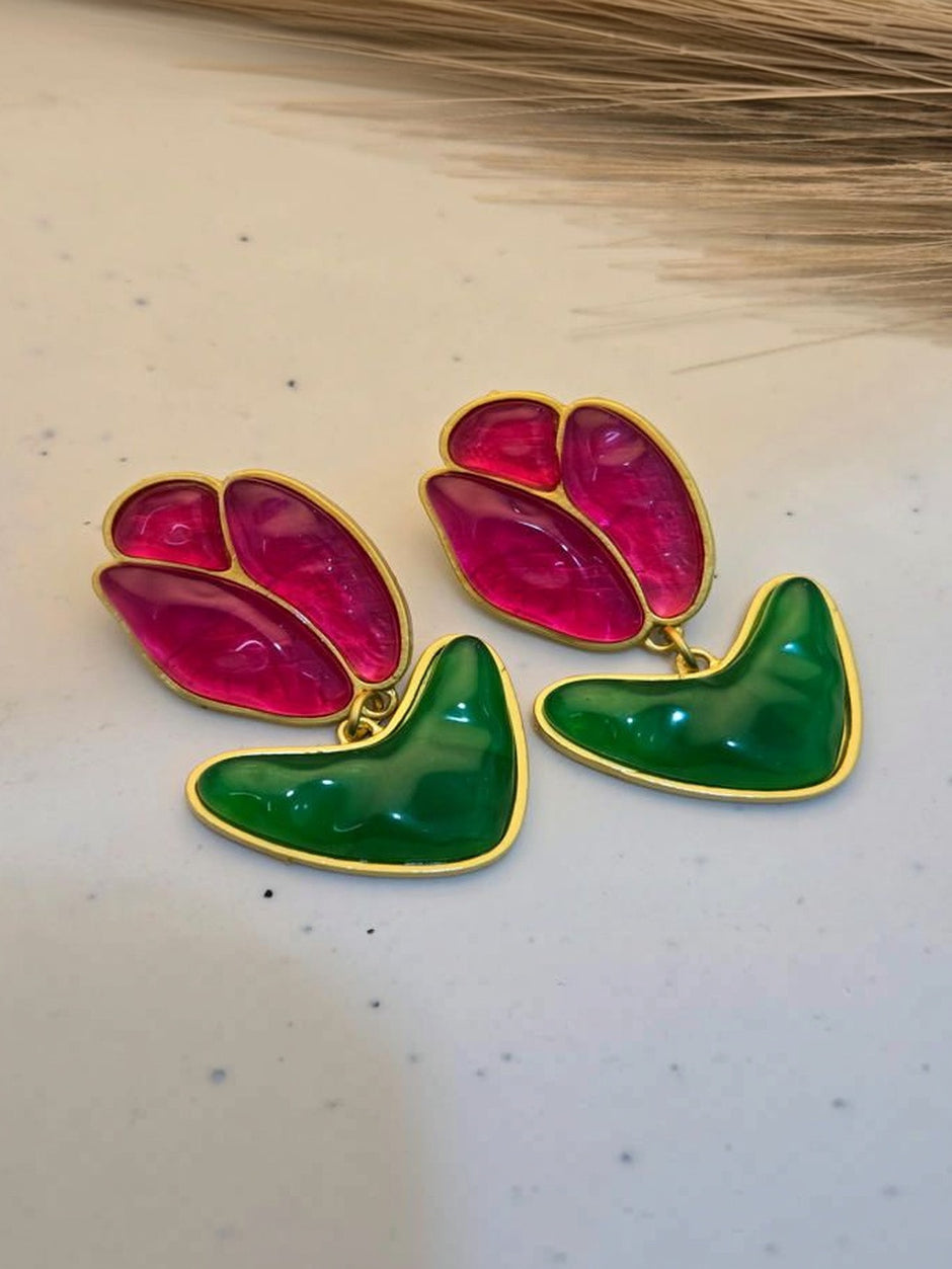 Pair of gold-toned tulip drop earrings with fuchsia resin petals and green leaf charms on a cream speckled surface