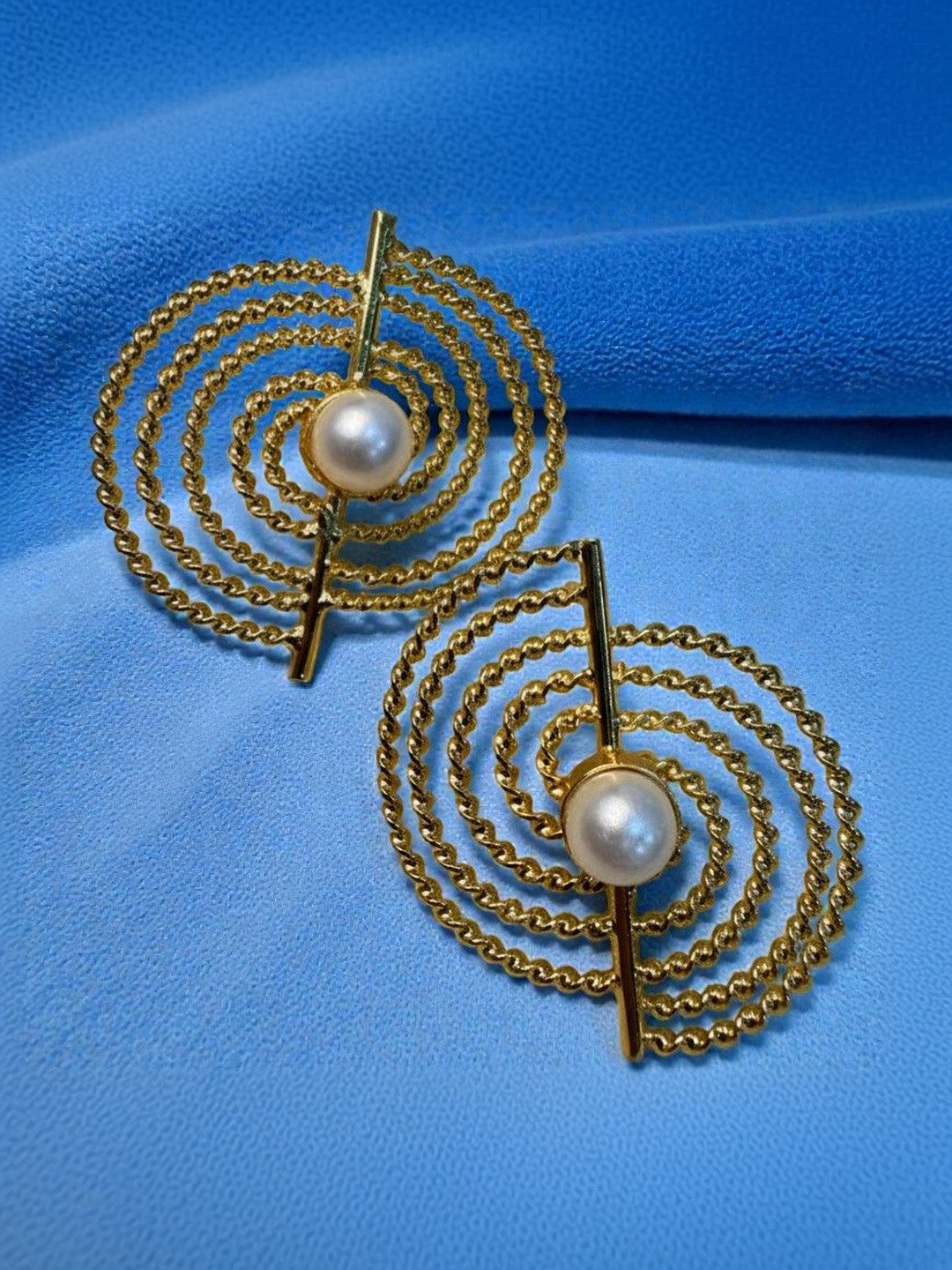 Pair of gold-plated concentric rope stud earrings with pearl centres on blue fabric