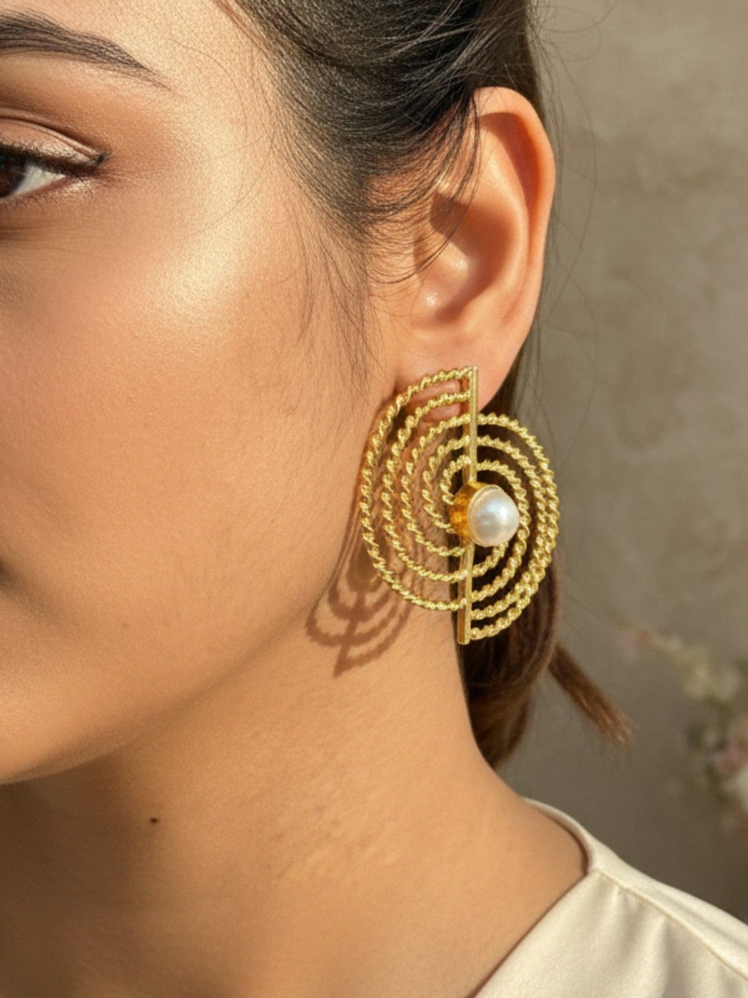 Woman wearing large gold spiral rope stud earring with pearl, shown on ear in profile