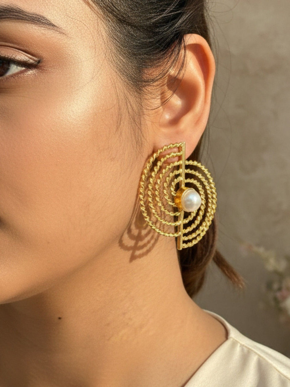 Woman wearing large gold spiral rope stud earring with pearl, shown on ear in profile