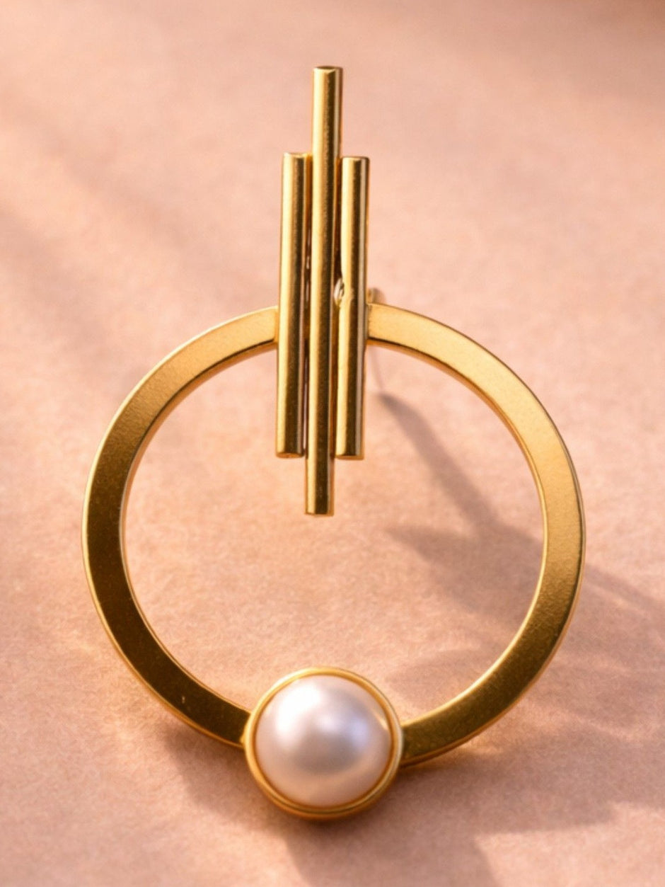 Single gold-plated hoop earring with triple-bar stud top and faux pearl at the base, on a pink surface