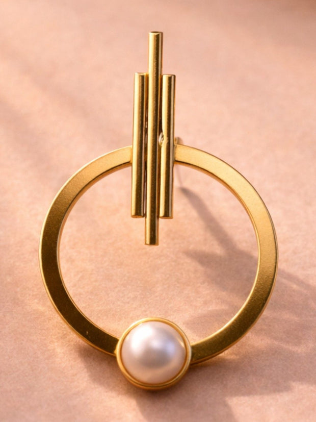 Single gold-plated hoop earring with triple-bar stud top and faux pearl at the base, on a pink surface