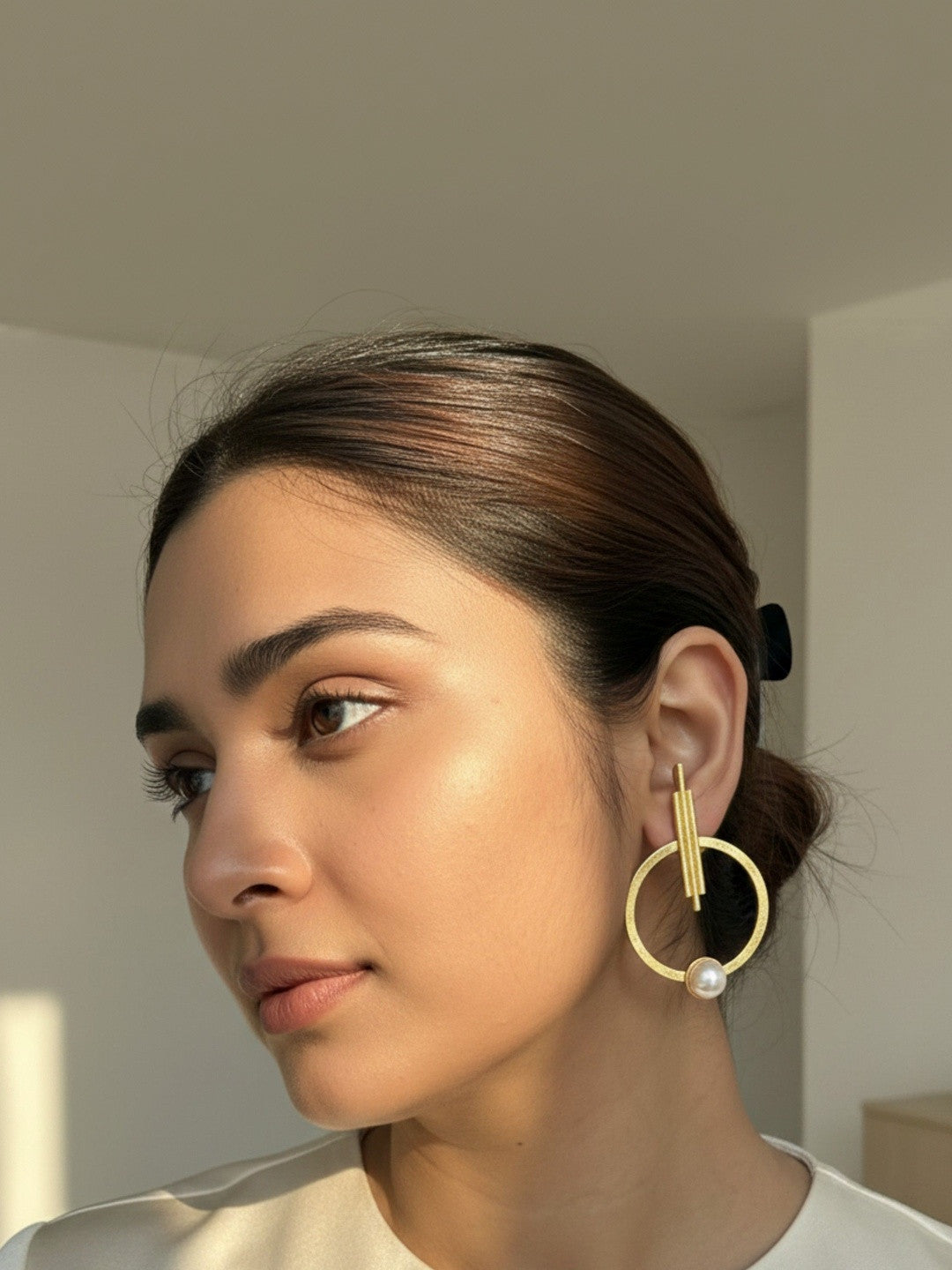 Woman with hair in a bun wearing a gold geometric hoop earring with pearl accent, side profile view