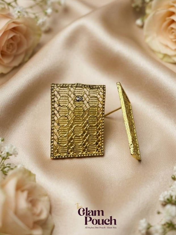 Pair of gold-toned filigree rectangle stud earrings on cream satin with blush roses