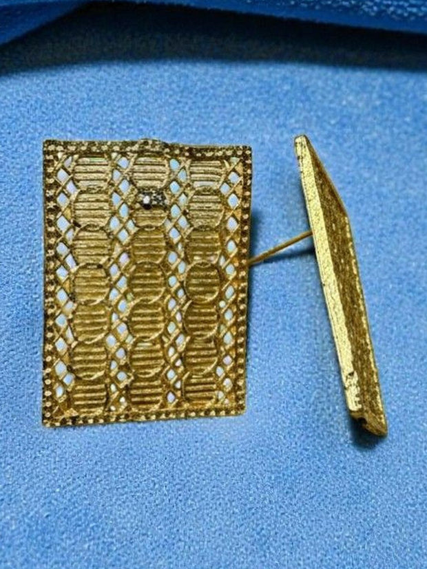 Close-up of gold filigree rectangle earring showing open lattice work on blue fabric