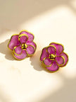 Close-up of gold-plated marbled pink enamel flower stud earrings on a warm cream surface with soft shadows