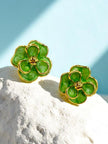 Pair of green marbled enamel floral stud earrings with gold-tone borders resting on white textured stone
