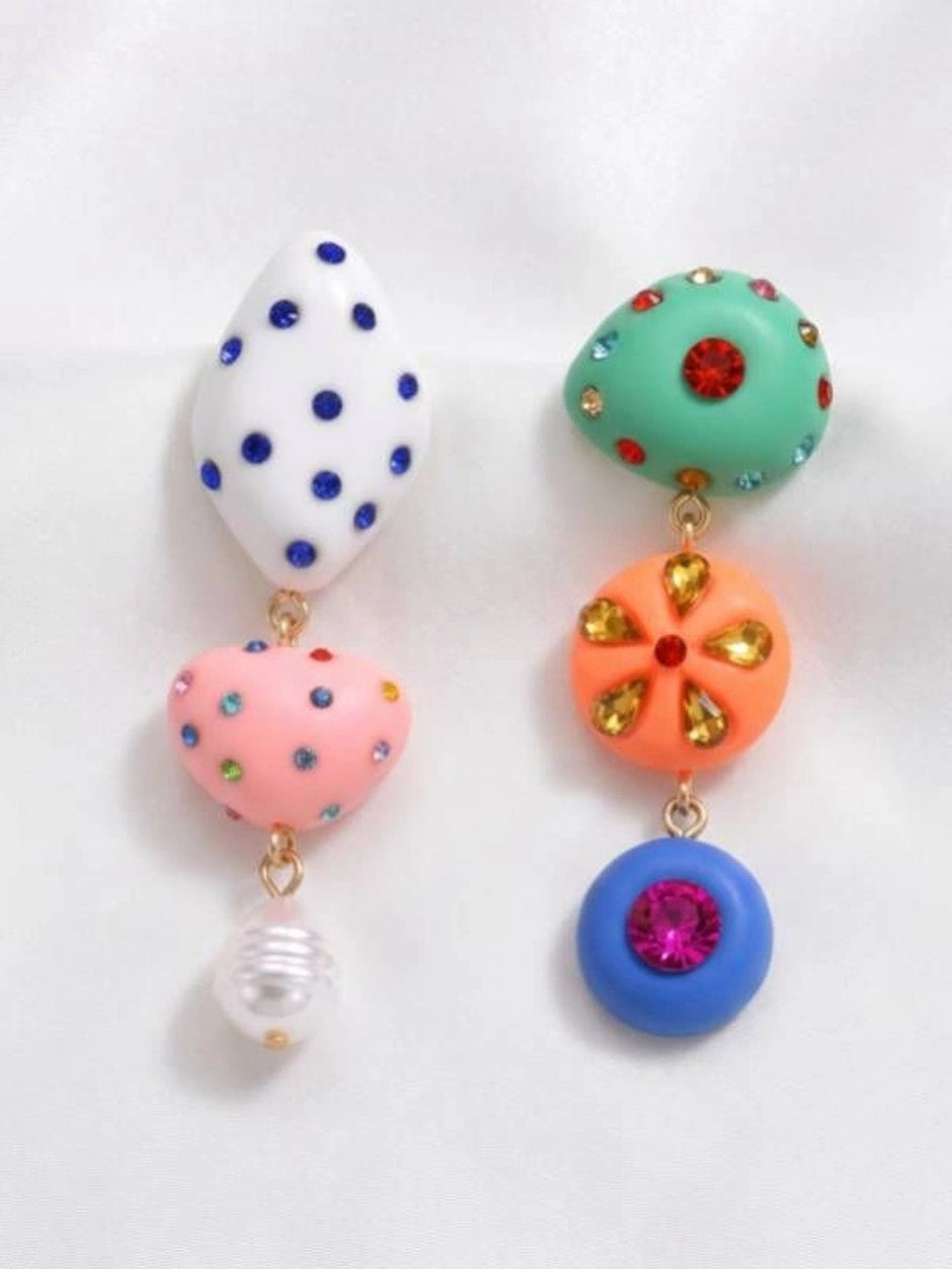 Pair of quirky drop earrings with white polka-dot oval, pink heart, pearl drop, teal dome, orange floral disc, and blue ring charms on white background