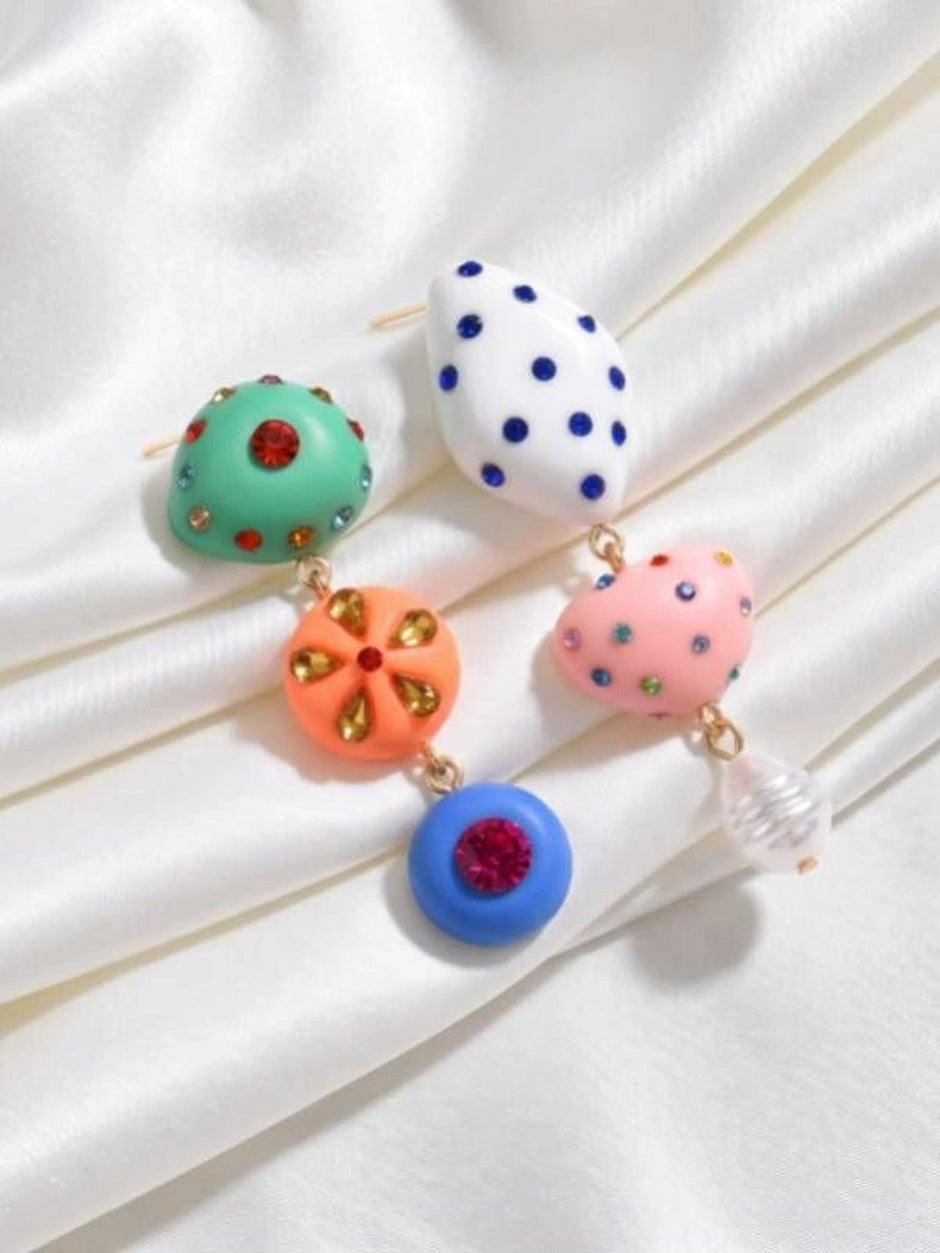 Both mismatched drop earrings laid flat on white satin showing rhinestone detailing on all resin charms and gold-toned connectors