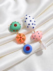 Both mismatched drop earrings laid flat on white satin showing rhinestone detailing on all resin charms and gold-toned connectors