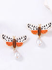 Pair of gold-toned moth earrings with white black enamel wings orange lower wings and baroque faux pearl drops on white background