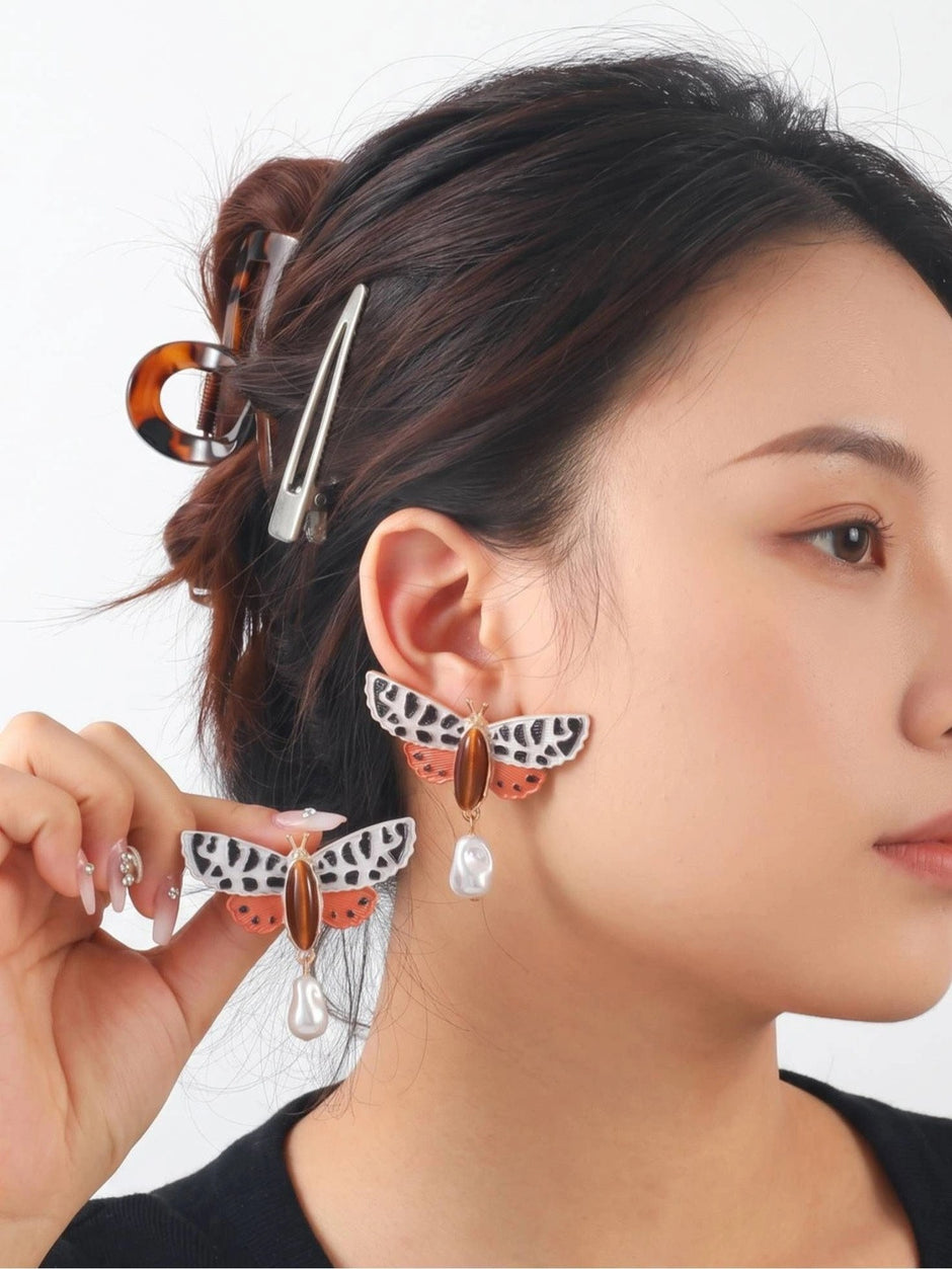 Close-up side view of woman wearing moth earring with pearl drop while holding second earring near ear
