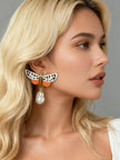 Blonde model wearing single large moth enamel drop earring with baroque pearl against grey background
