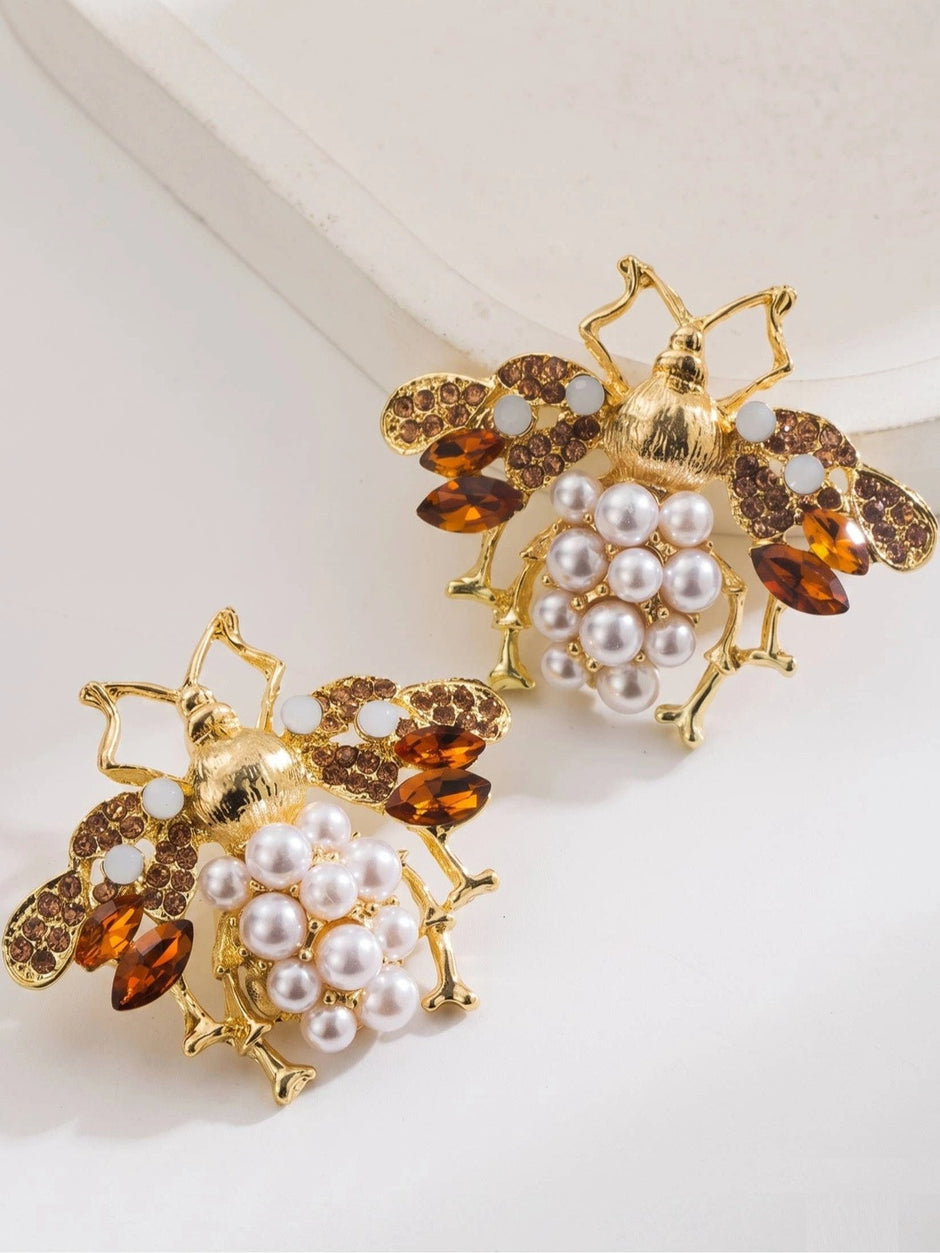 Two gold-toned honeybee stud earrings with faux pearl bodies and amber crystal wings displayed on white surface