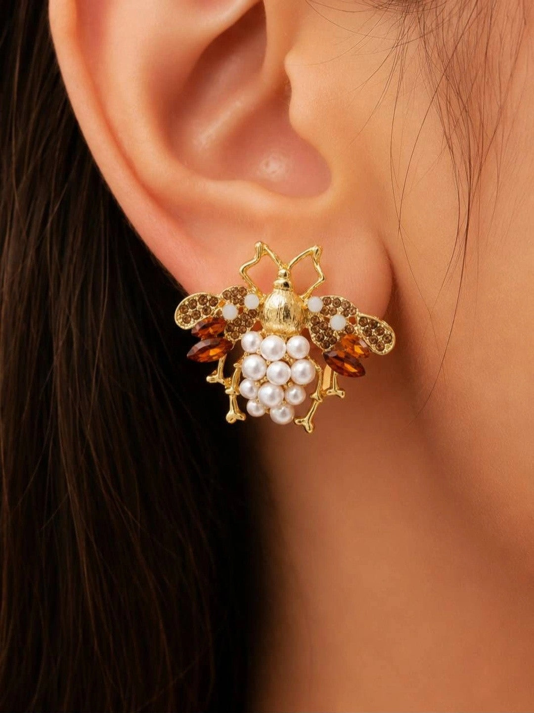 Close-up side view of gold bee earring with pearl cluster abdomen and amber crystal wings worn on a woman's ear