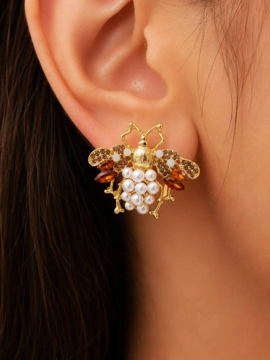 Close-up side view of gold bee earring with pearl cluster abdomen and amber crystal wings worn on a woman's ear