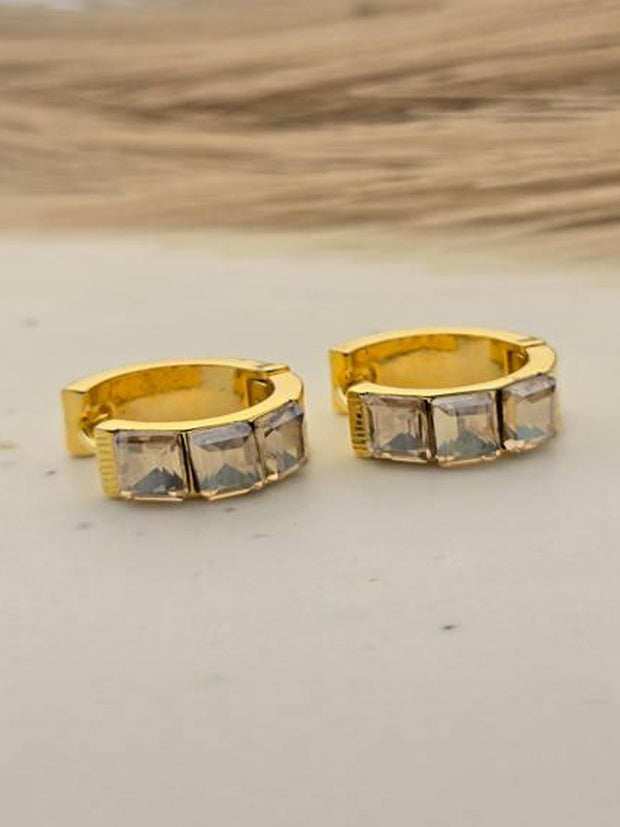 Pair of gold-plated huggie hoop earrings with two square CZ stones on marble surface