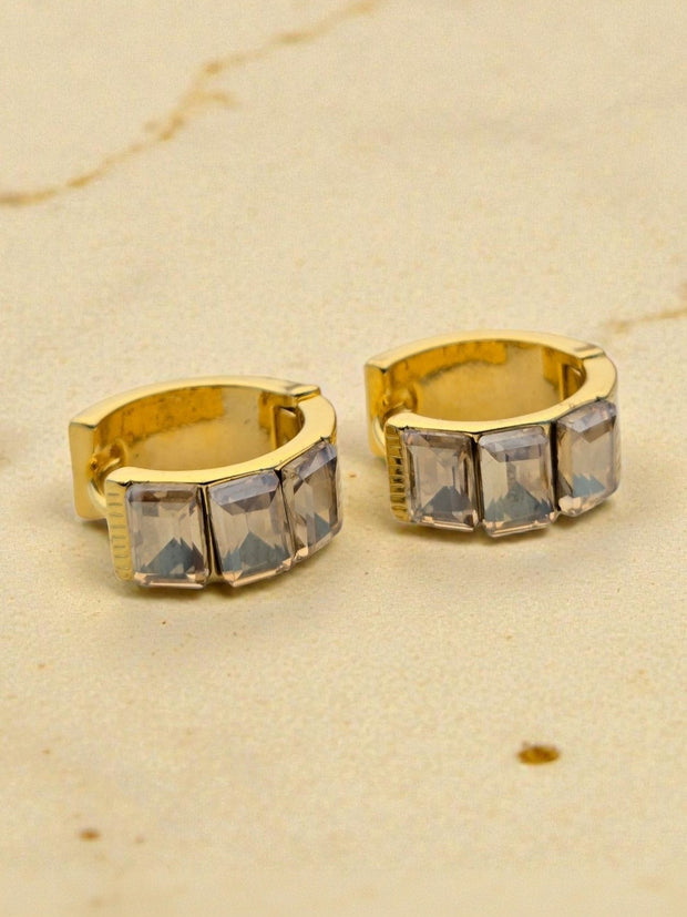 Close-up of gold huggie hoops showing square cubic zirconia stone detail on cream marble