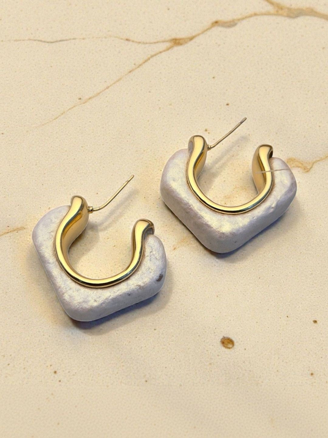 Close-up of two pearlescent resin square hoop earrings showing gold inner hoop detail on marble surface