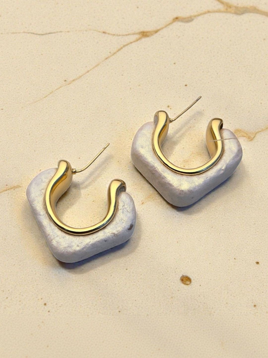 Close-up of two pearlescent resin square hoop earrings showing gold inner hoop detail on marble surface