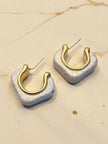 Close-up of two pearlescent resin square hoop earrings showing gold inner hoop detail on marble surface