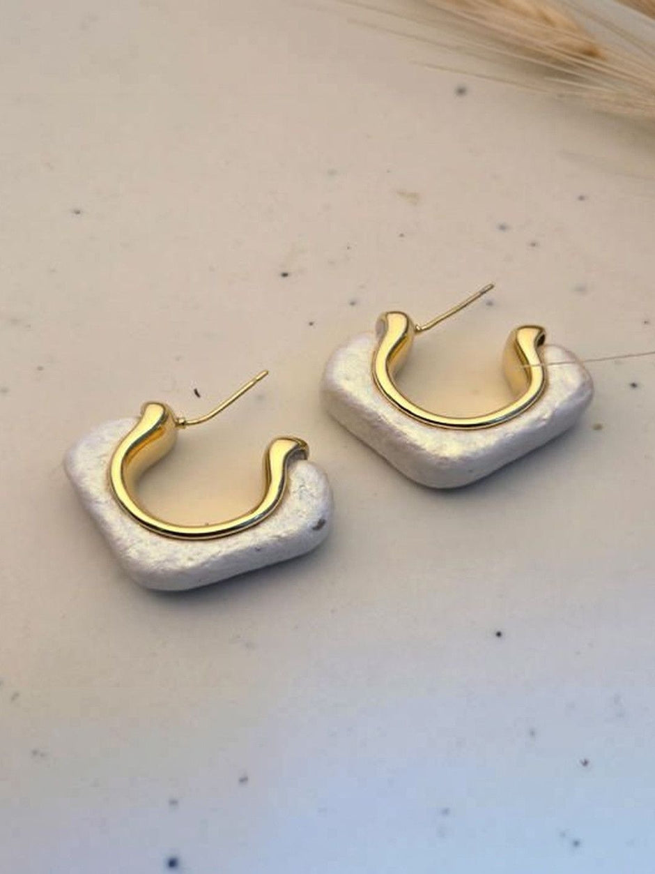 Two pearlescent white resin hoop earrings with polished gold inner hoop displayed on white speckled surface