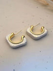 Two pearlescent white resin hoop earrings with polished gold inner hoop displayed on white speckled surface