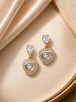 Pair of gold-plated heart drop earrings laid flat on a champagne satin surface