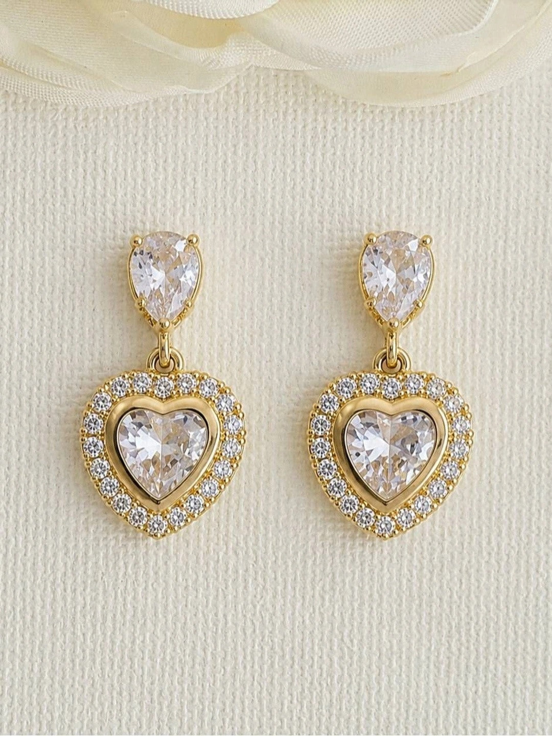 Pair of gold-plated heart CZ drop earrings displayed upright against a white textured background