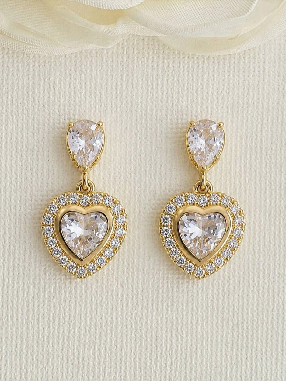 Pair of gold-plated heart CZ drop earrings displayed upright against a white textured background