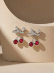 Pair of silver-tone crystal cherry bow drop earrings resting on a curved beige display prop