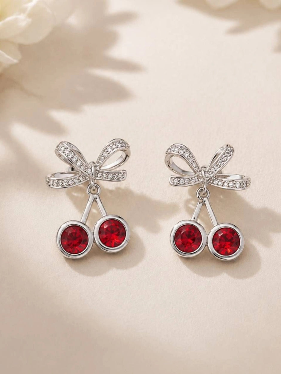 Close-up front view of both cherry bow drop earrings laid on a white floral surface