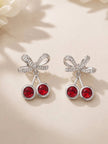 Close-up front view of both cherry bow drop earrings laid on a white floral surface
