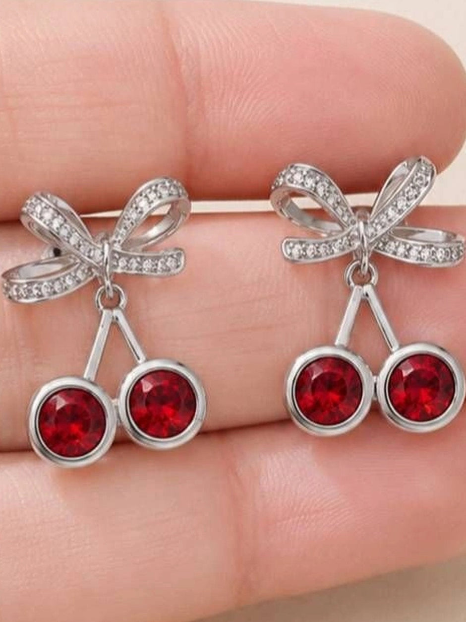 Both cherry bow drop earrings held in an open palm showing scale and red crystal detail